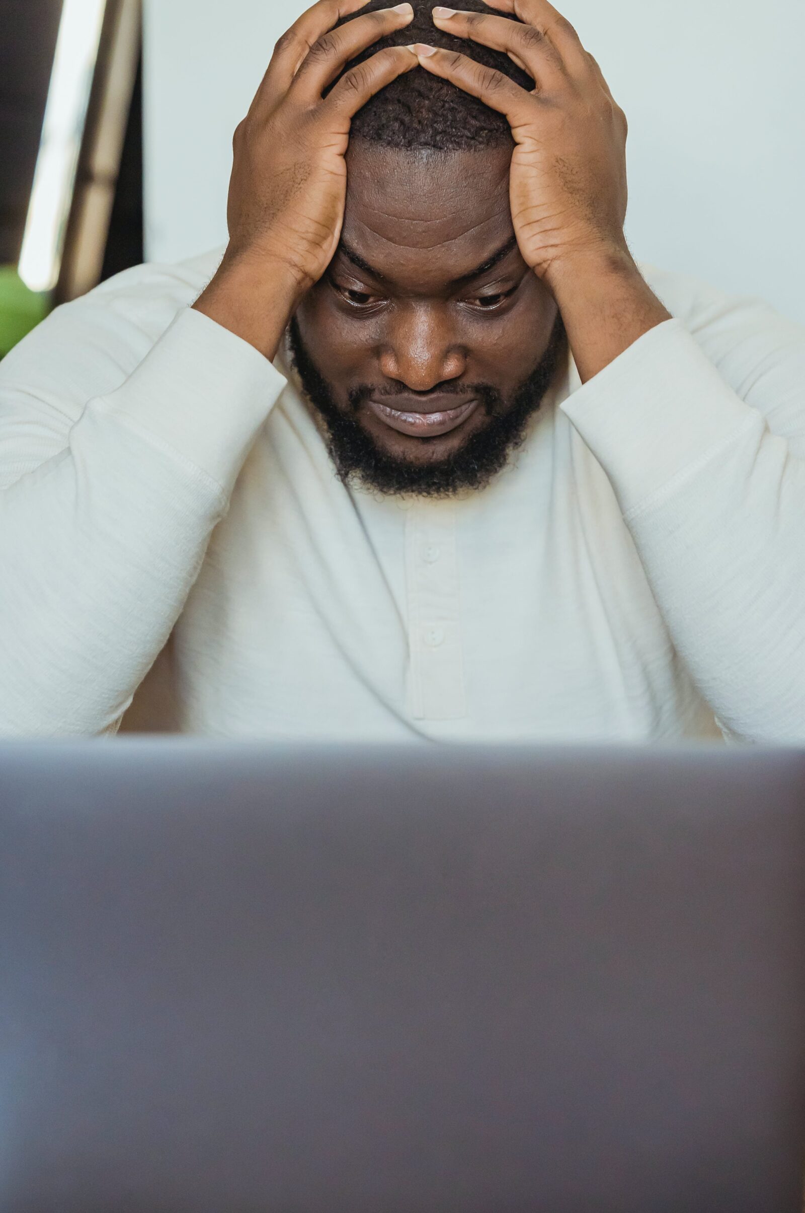 Sad black man with hands on head near laptop