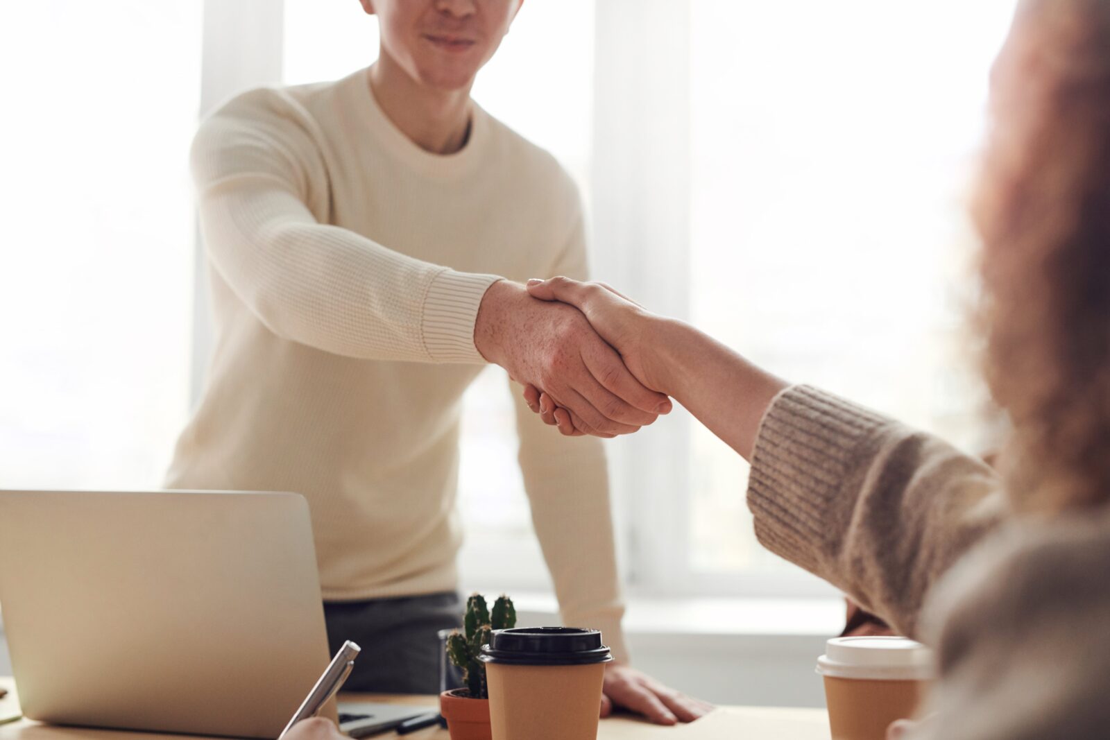 Man and woman demonstrating partnership by shaking hands across office desk
